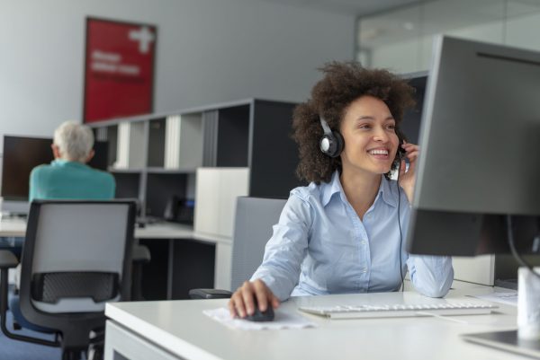 Photo of smiling, Cheerful mixed-race girl call working in center operator, wearing business attire. Young Customer service executive woman working at office. Female Customer service executive talking on headset in office. Young attractive friendly customer service answering customer questions on the telephone with toothy smile.